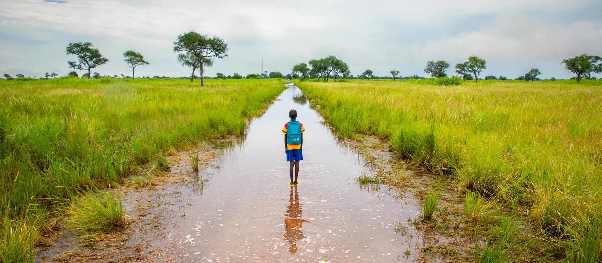Child standing in a field with flooding